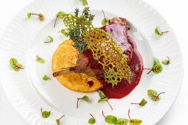 Beyaz tabakta kırmızı böğürtlen soslu patates pirzolası ile fırında ördek bacağı. 