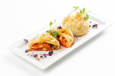 Domatesli fırınlanmış çörekler ve beyaz tabakta yeşillikle süslenmiş peynir. 