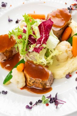 Patates püresi, sebze ve beyaz tabakta kırmızı soslu et madalyonları. 