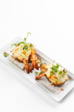 Krem peynir sosunun altında karides ve beyaz tabakta yeşil patates dilimleri. 