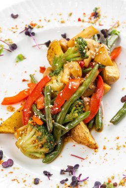 Kızarmış patates ve kırmızı biber dilimli yeşil fasulye. Beyaz tabakta sos. 