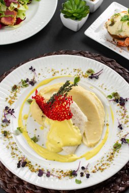 Fırında balık fileto ve krema soslu patates püresi ve otlarla süslenmiş ton balığı dilimleri ve beyaz tabakta kırmızı kraker. 