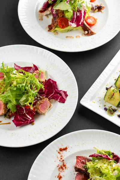 yeşil ve kırmızı salata tabakları ton balığı dilimleri, somon balığı ve domatesler gri masa arkasında