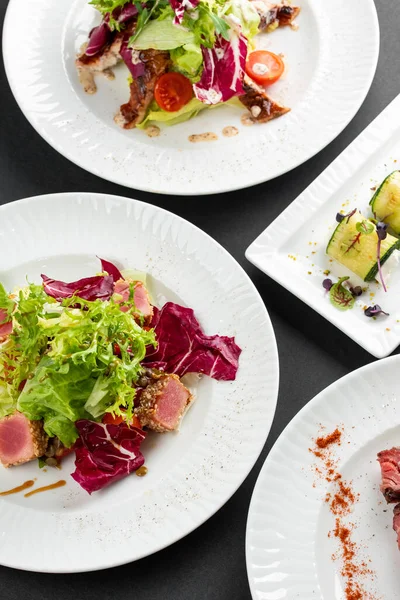 yeşil ve kırmızı salata tabakları ton balığı dilimleri, somon balığı ve domatesler gri masa arkasında