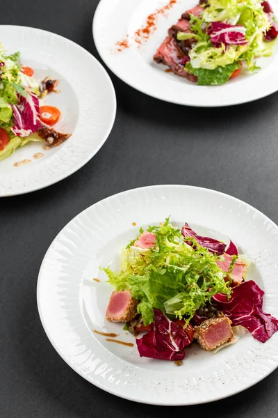 yeşil ve kırmızı salata tabakları ton balığı dilimleri, somon balığı ve domatesler gri masa arkasında