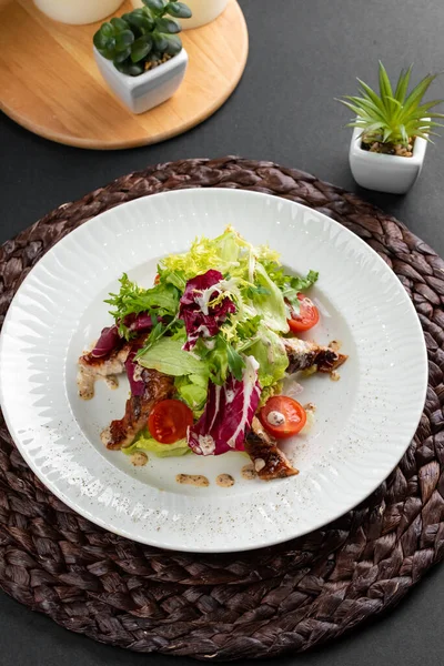 Renkli lezzetli salata, fırında somon, yeşillik ve domatesler kırsal ahşap peçetede beyaz tabakta. 