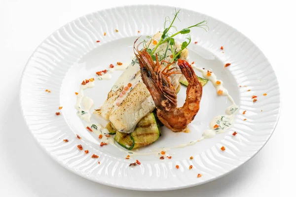 fish fillet with grilled zucchini and shrimp with lemon butter sauce on white plate