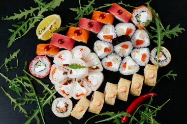Kırmızı somon, karides ve siyah tabakta krem peynirli füme yılan balığı ile farklı Asya suşi dürümleri.
