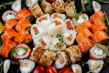 Farklı lezzetli suşi ruloları somon, karides ve krem peynirli füme yılan balığı siyah tabakta.