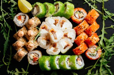 Somon balığı, karides ve siyah tabakta krem peynirli füme yılan balığı ile renkli suşi ruloları.