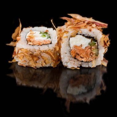 Somon balıklı suşi ruloları ve siyah masa arkasında krem peynirli beyaz pirinç.