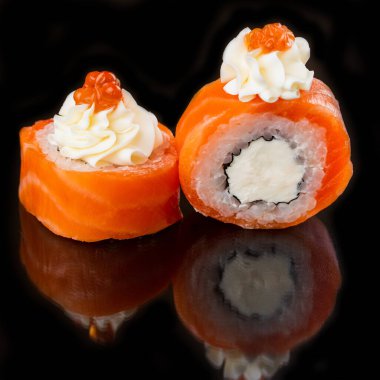 Somon balıklı suşi ruloları ve siyah masa arkasında krem peynirli beyaz pirinç.