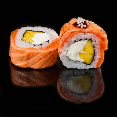 Somon balıklı suşi ruloları ve siyah masa arkasında krem peynirli beyaz pirinç.