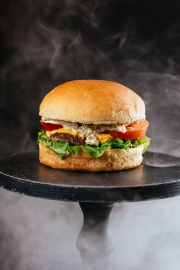 Tavuklu ızgara hamburger, beyaz altın çörekler, domatesler, yeşil salata ve siyah ahşap masa arkasında kızarmış tavuk yumurtası.
