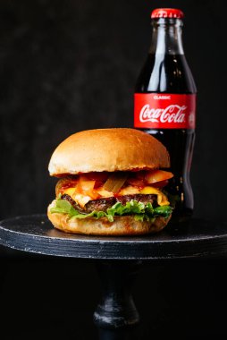 Beyaz çörekler peynirli et burger ve siyah masa arkasında Coca Cola şişeli pastırma.
