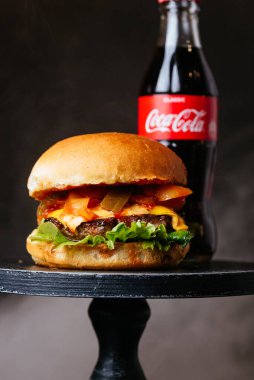 Beyaz çörekler peynirli et burger ve siyah masa arkasında Coca Cola şişeli pastırma.