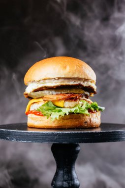 Siyah masa arkasında peynirli, soğanlı ve salata yapraklı duble et burger.