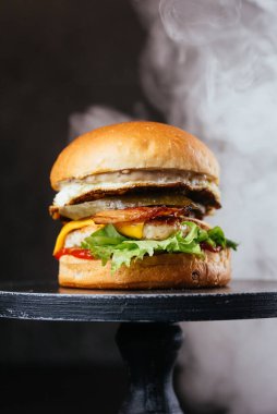 Siyah masa arkasında peynirli, soğanlı ve salata yapraklı duble et burger.