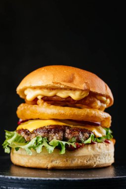 Siyah masa arkasında peynirli, soğanlı ve salata yapraklı duble et burger.