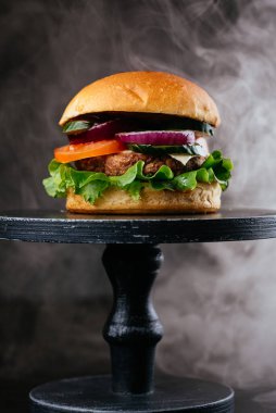 Tahta arka planda beyaz çörekler, domatesler, soğanlar ve yeşil salata yapraklarıyla sulu ızgara et burger.