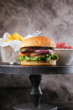 Taze ızgara hamburgerli ahşap masa metal sepette patates kızartması ve siyah arka planda sos tabağı.