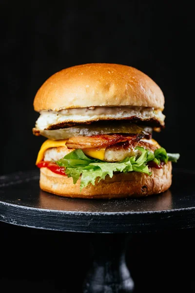 Siyah masa arkasında peynirli, soğanlı ve salata yapraklı duble et burger.