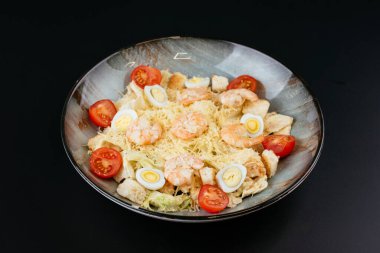 Karidesli Sezar salatası, kiraz domatesleri, kızarmış ekmekler, romaine yaprakları ve yumurtalar mavi tabakta servis ediliyor ve soslu peynir.