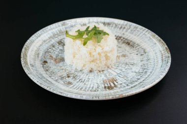 Pişmiş pirinç tabağı, siyah masada yeşil roka filizi ile servis edilir. 