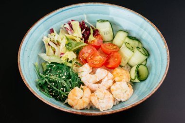 Karidesli yeşil salata ve siyah arka planda mavi tabakta domates.