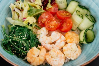 Karidesli yeşil salata ve siyah arka planda mavi tabakta domates.