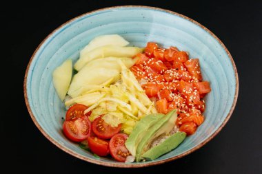 yeşil salata ile somon ve elma parçaları ile mavi tabakta siyah arka planda domates