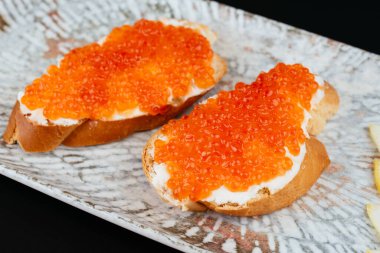 Tereyağlı ekmek ve gri tabakta limon dilimli kırmızı havyar. 