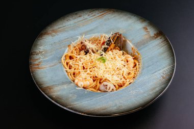 Siyah arka planda mavi tabakta deniz ürünleri ve peynirli makarna