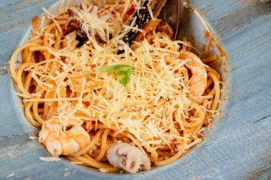 Siyah arka planda mavi tabakta deniz ürünleri ve peynirli makarna