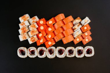 Somon balığı, karides ve krem peynirli füme yılan balığı ile siyah tabakta farklı renkte suşi ruloları.