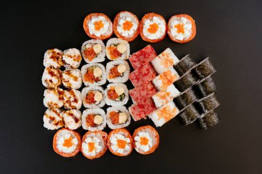 Somon balığı, karides ve krem peynirli füme yılan balığı ile siyah tabakta farklı renkte suşi ruloları.