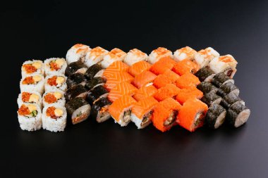 Somon balığı, karides ve krem peynirli füme yılan balığı ile siyah tabakta farklı renkte suşi ruloları.
