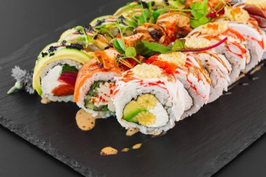 Somon balığı, sebze ve siyah tabakta krem peynirli beyaz pirinç ile hazırlanmış suşi ruloları.