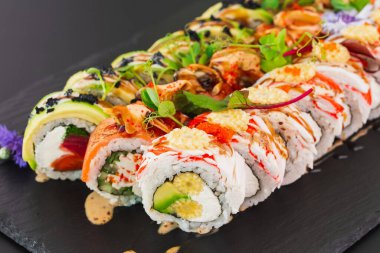 Somon balığı, sebze ve siyah tabakta krem peynirli beyaz pirinç ile hazırlanmış suşi ruloları.