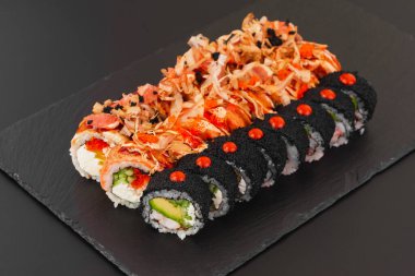 Somon balığı, sebze ve siyah tabakta krem peynirli beyaz pirinç ile hazırlanmış suşi ruloları.