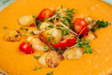 Siyah arka planda mavi tabakta servis edilen deniz tarağı kremalı çorba.