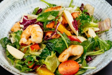 Mavi tabakta karides, yeşil ve domatesli renkli salata.