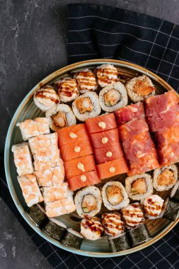 Farklı suşi ruloları, kırmızı somon balığı, karides ve siyah tabakta krem peynirli füme yılan balığı.