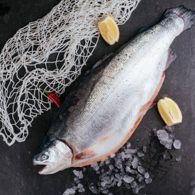 Siyah tabakta taze çiğ balık ve masada baharatlar.