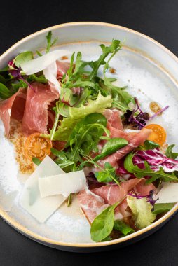 Peynirli prosciutto dilimlenmiş taze yeşil salata ve masa arkasında beyaz tabakta domates.