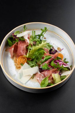 Peynirli prosciutto dilimlenmiş taze yeşil salata ve masa arkasında beyaz tabakta domates.