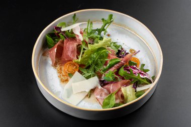 Peynirli prosciutto dilimlenmiş taze yeşil salata ve masa arkasında beyaz tabakta domates.