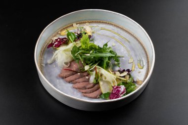 Masa arkasındaki beyaz tabakta et parçaları olan yeşil salata.