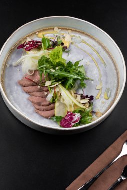 Masa arkasındaki beyaz tabakta et parçaları olan yeşil salata.