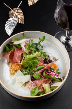 Beyaz tabak yeşil salata ve arka planda kırmızı şarap kadehi olan et dilimleri.